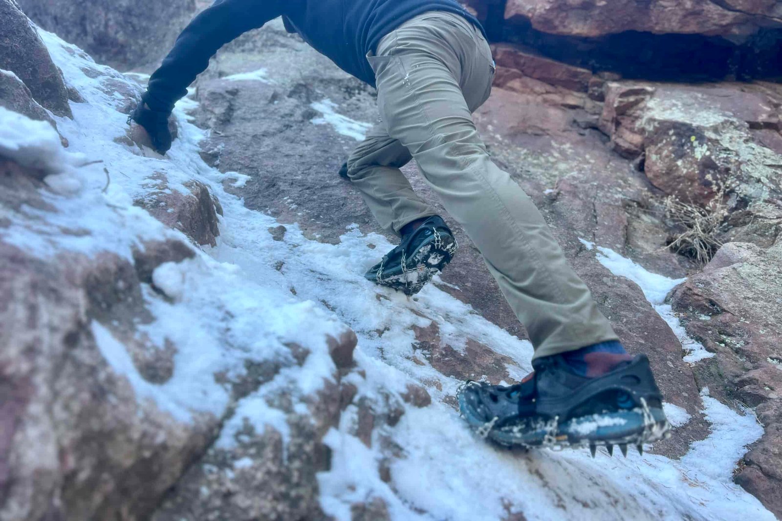 A hiker scales an icy rock face with a pair of ice spikes.