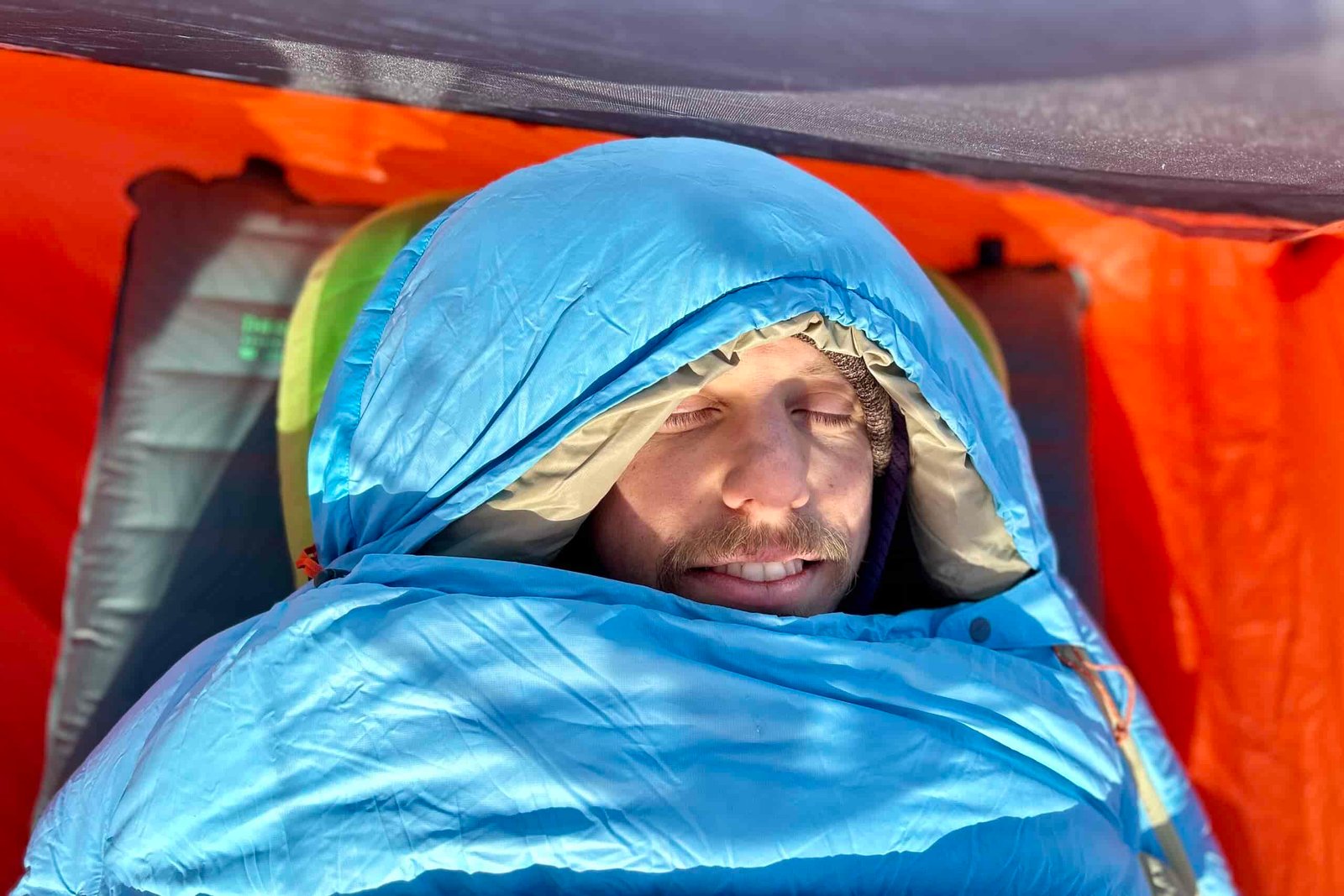 Image from above of a man in a sleeping bag with the hood up.