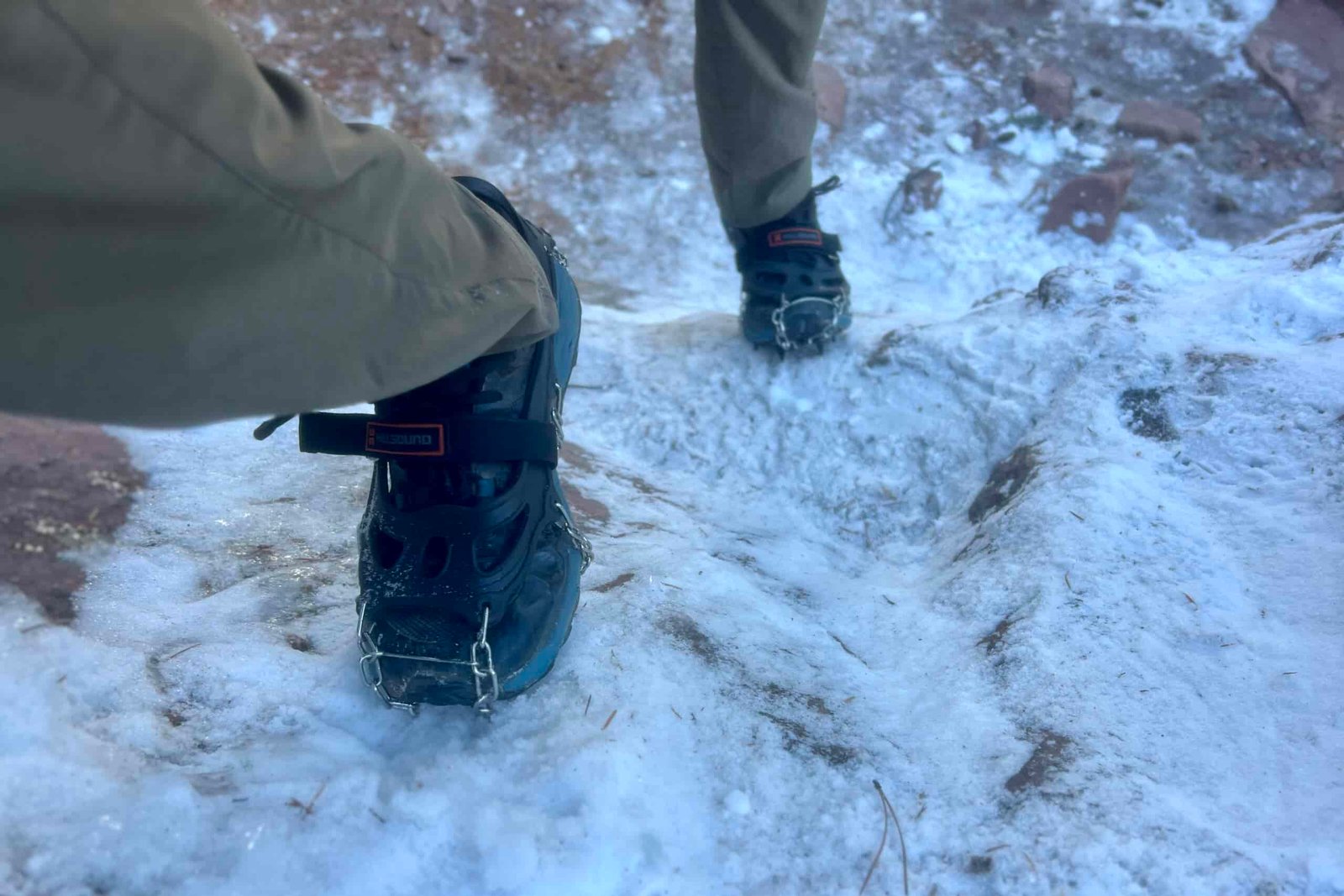 POV view of a hiker scaling an icy rock face with a pair of ice spikes.