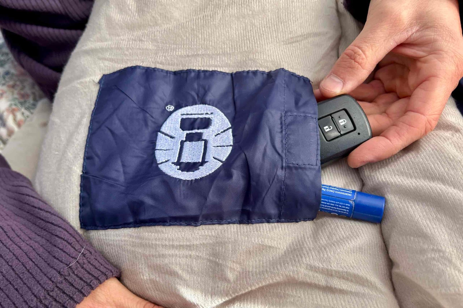 Close up image of a person's hands pulling car keys and a chapstick out of a sleeping bag's internal stash pocket.