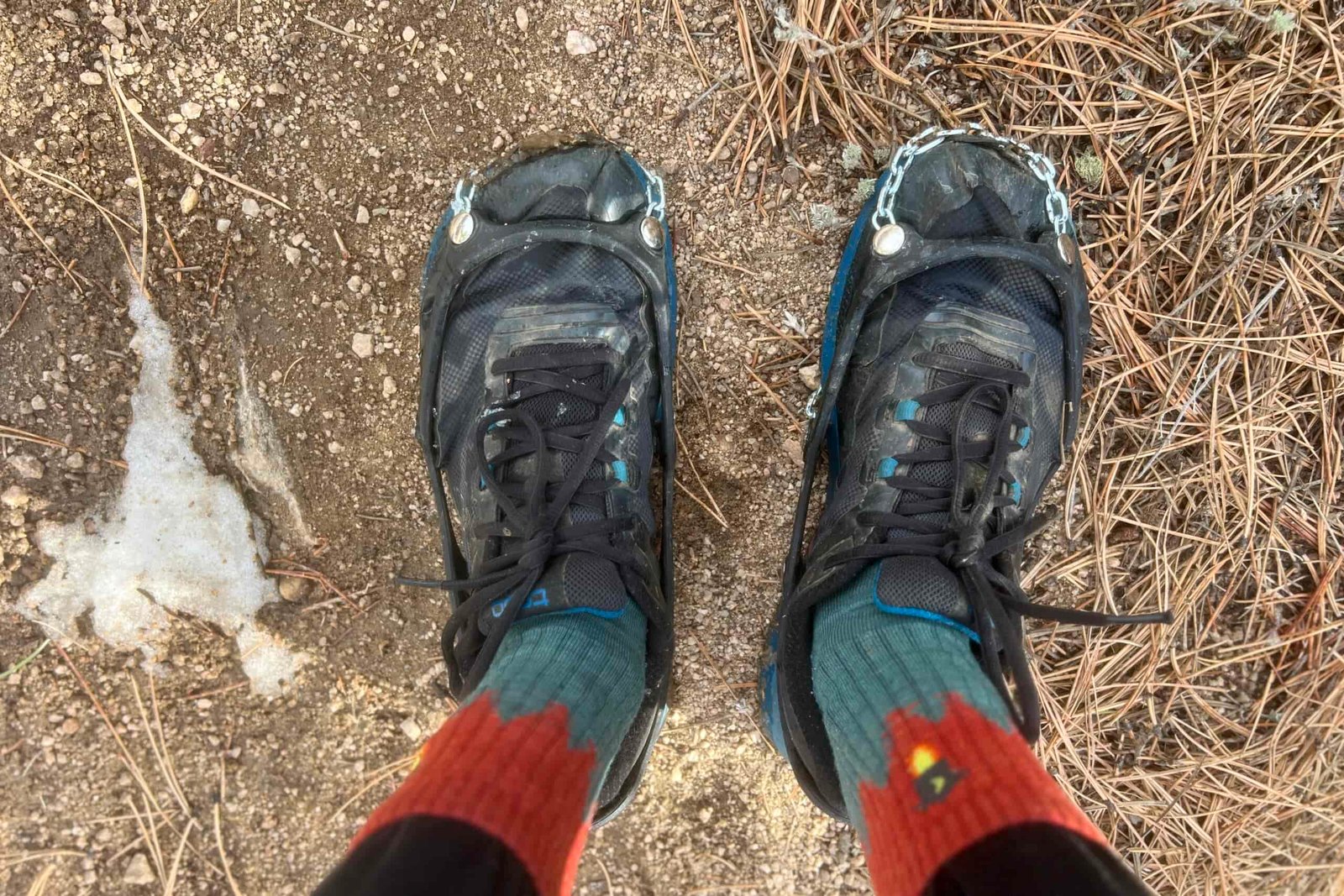 A POV view of a hiker looking down at his shoes that are wearing a pair of ice cleats.