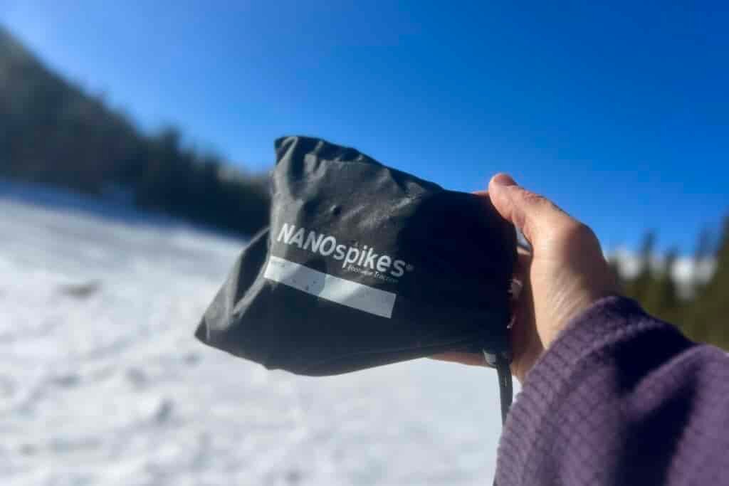 A hand holds out a stuff sack for a pair of ice cleats against a blue sky and snowy background.