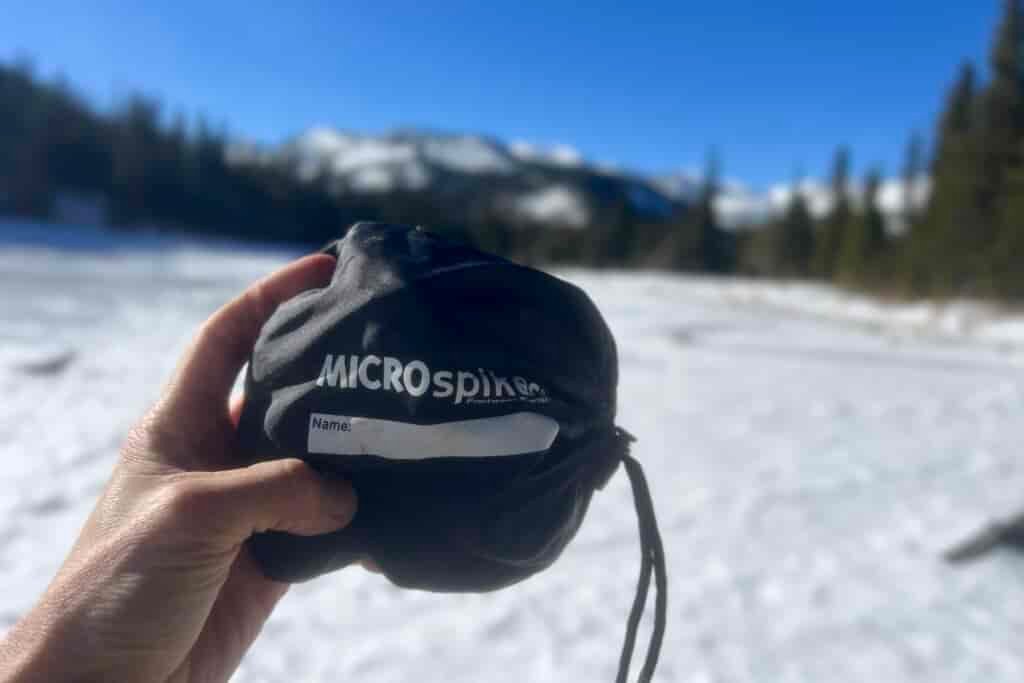 A hand holds a stuff sack for ice cleats against a blue sky and snowy background.