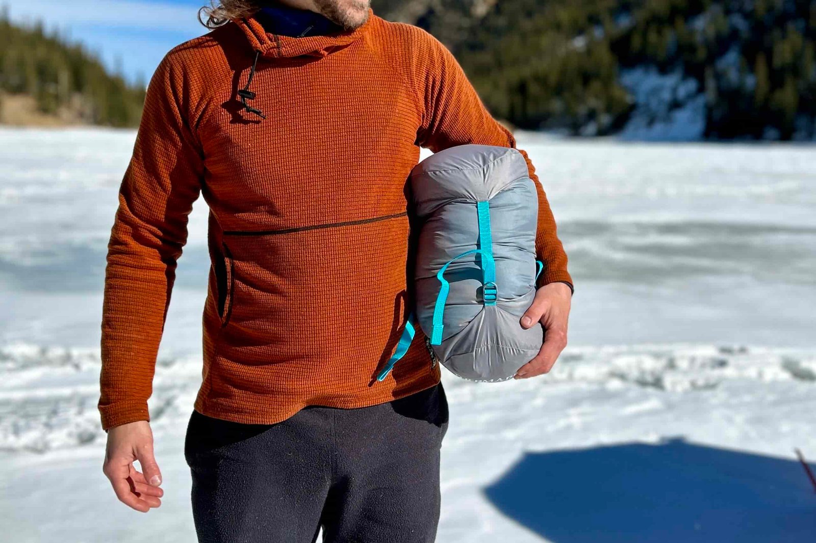 Close up image of a man with a sleeping bag stuff sack under his arm in a wintry setting.