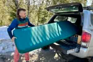 A man slides a large camping mattress into the back of a truck.