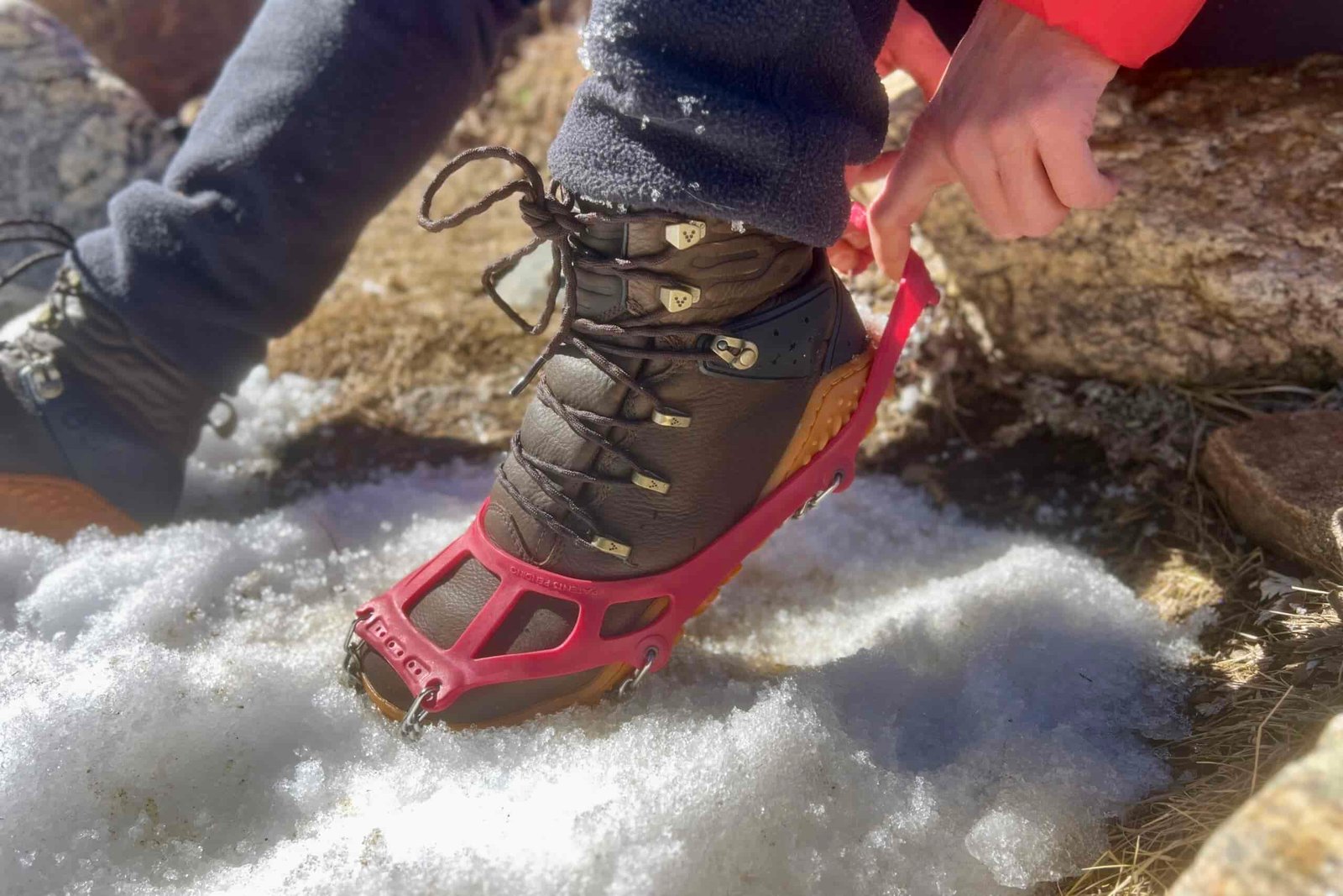 A close up of a hiker pulling a pair of ice cleats onto his boots.