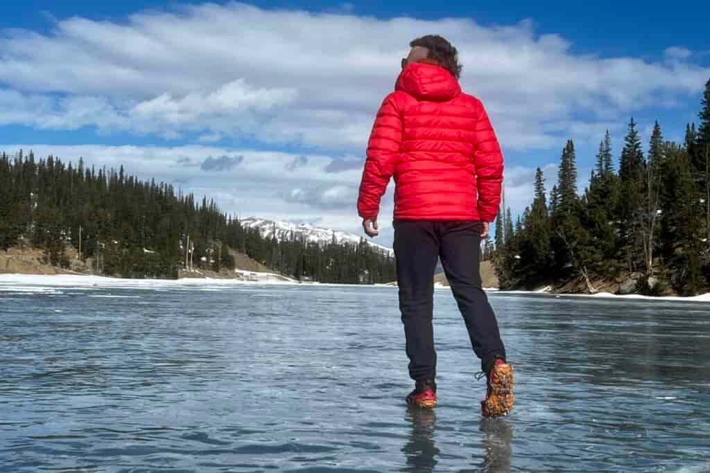A hiker walks away from the camera on a frozen lake while wearing a pair of ice cleats.