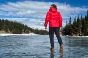 A hiker walks away from the camera on a frozen lake while wearing a pair of ice cleats.