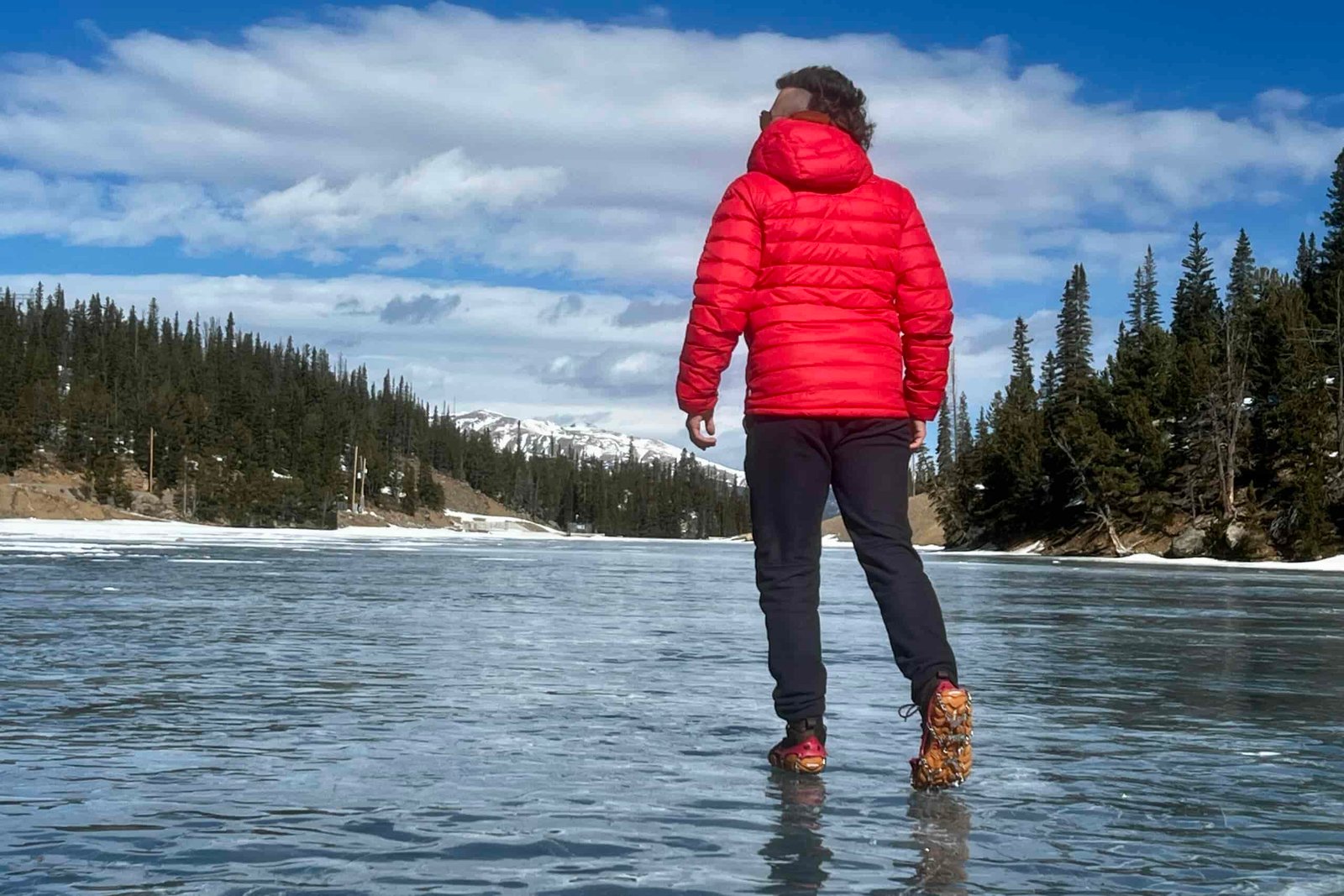 A hiker walks away from the camera on a frozen lake while wearing a pair of ice cleats.