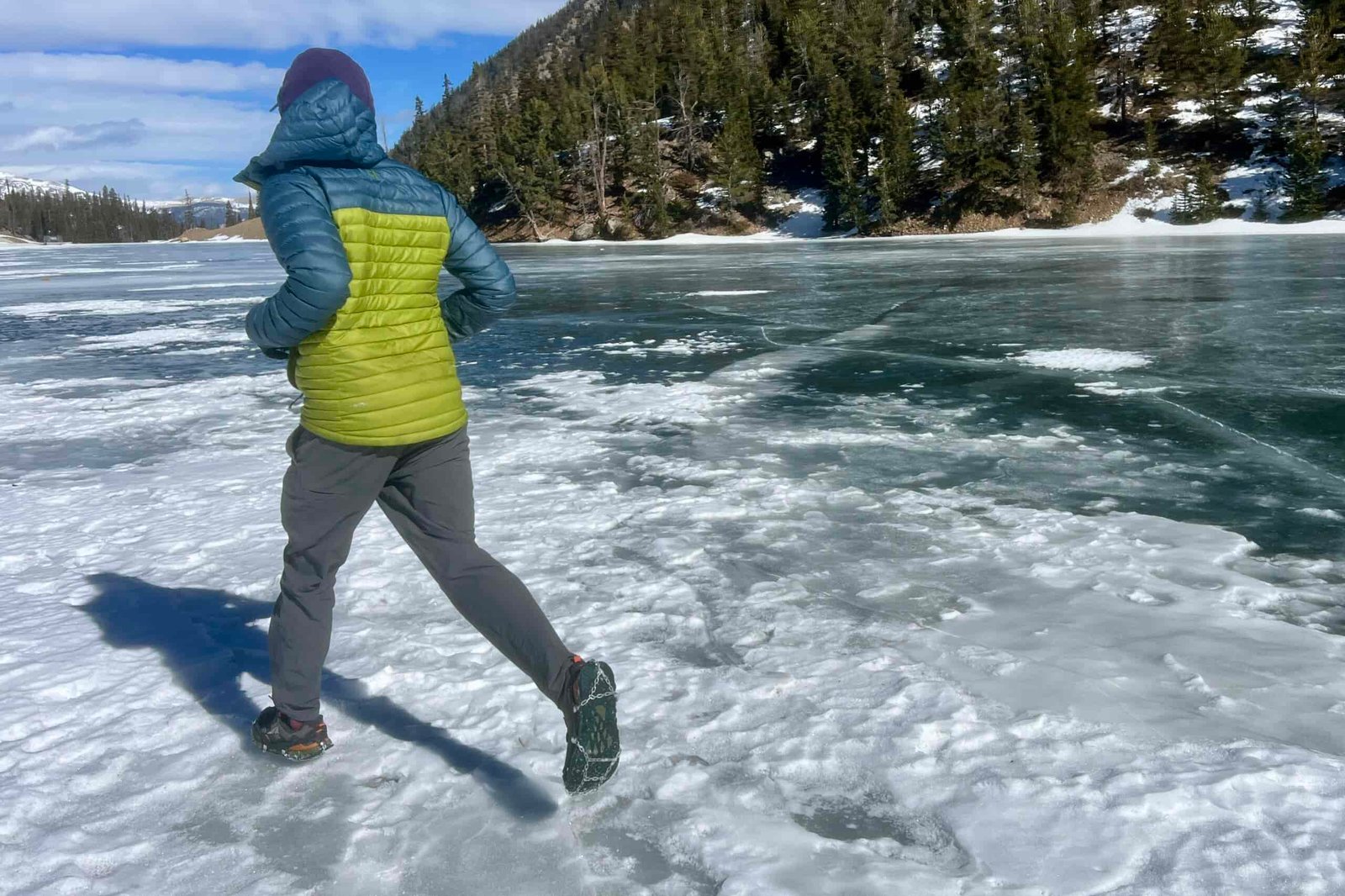 A hiker walks away on a frozen lake, showing the bottom of his shoe which is wearing an ice cleat.