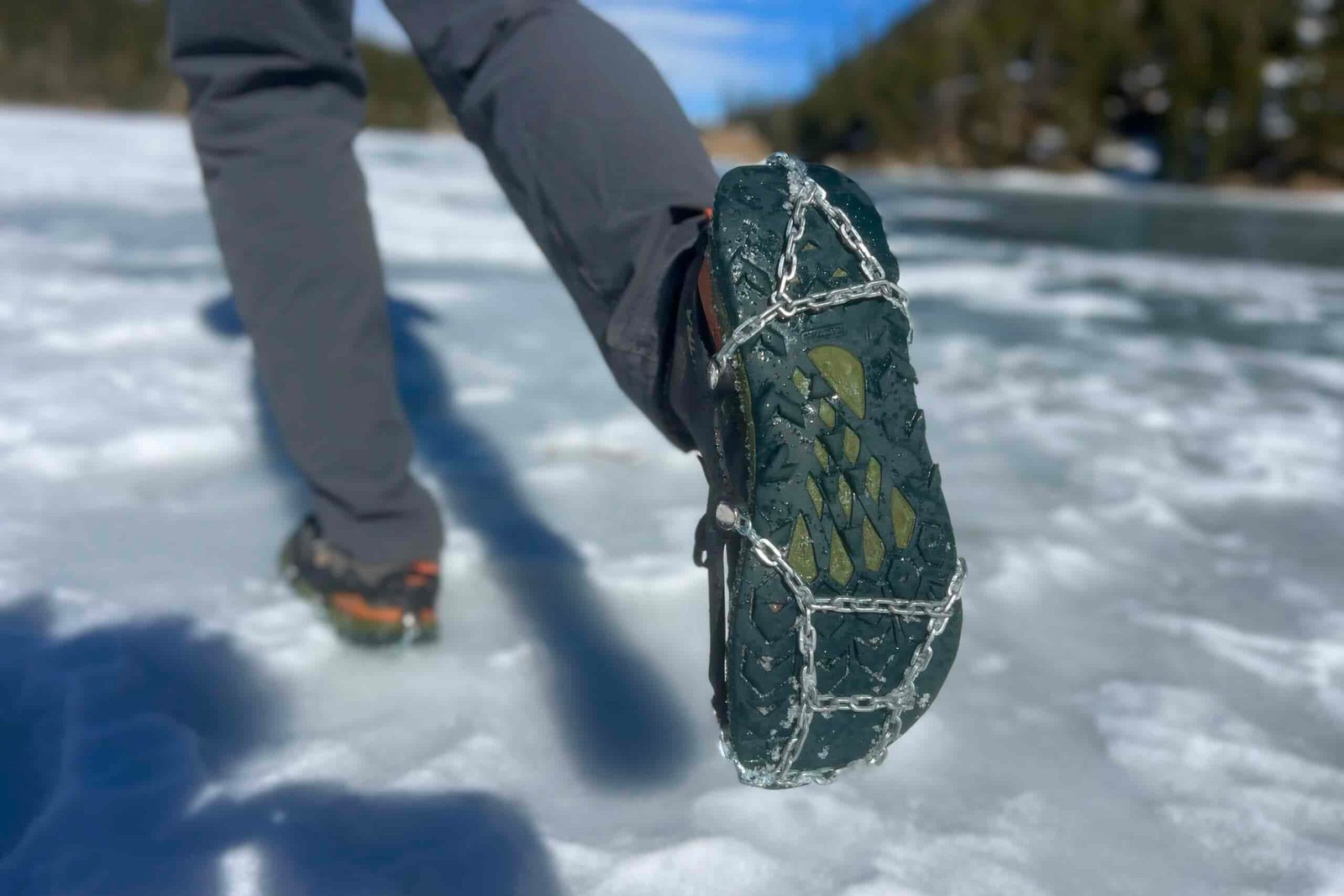 A hiker walks away on snow, showing the bottom of his shoe which is wearing an ice cleat.