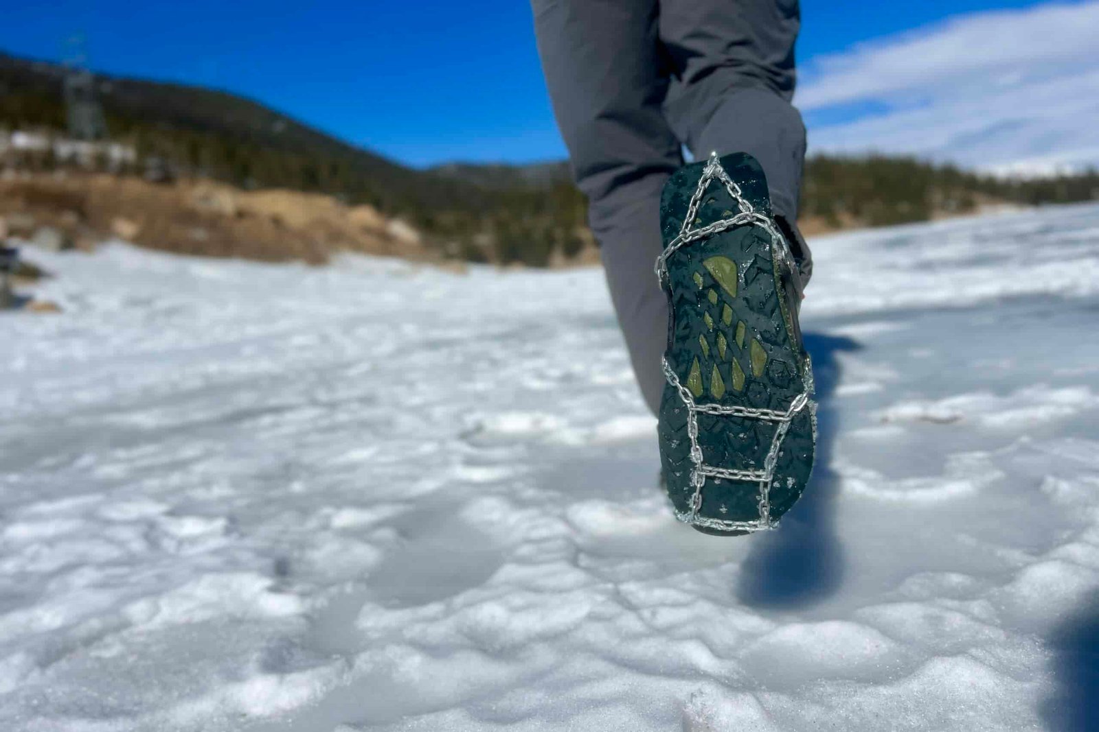 A hiker walks away on snow, showing the bottom of his shoe which is wearing an ice cleat.