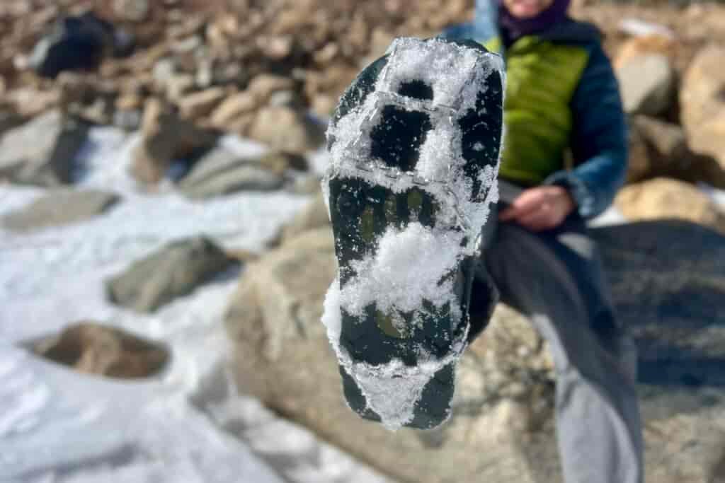 A hiker showing the bottom of his shoe which has an ice cleat caked with snow.