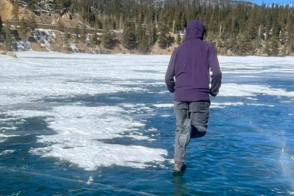 A person runs away from the camera on a frozen lake wearing a pair of ice cleats.