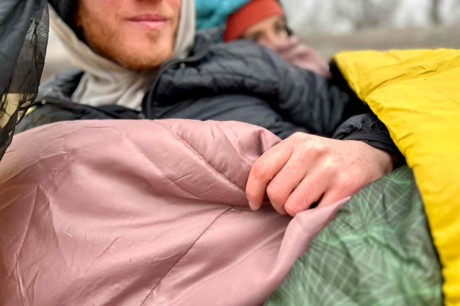 Close-up image of a person resting in a sleeping bag with their hand on the internal blanket.