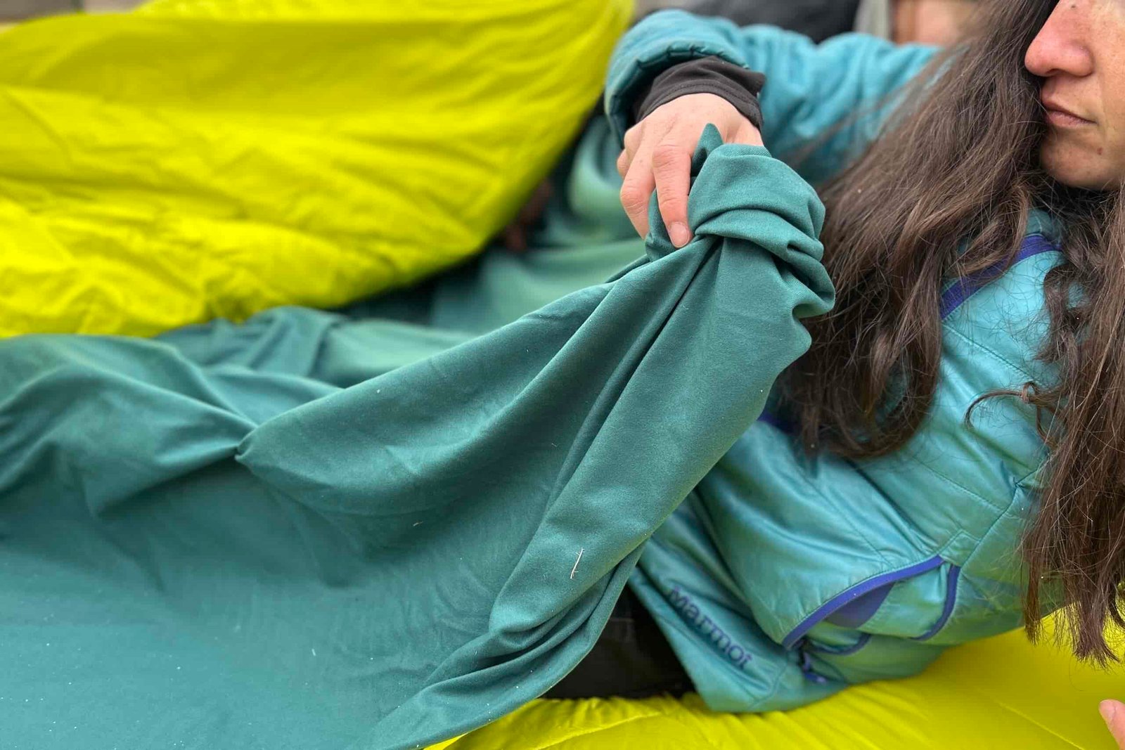 Close up image of a woman pulling the interior blanket of a double sleeping bag over her body.