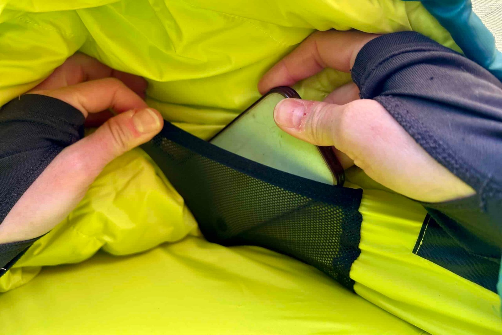 Close up image of two hands pulling a phone out of a sleeping bag's interior stash pocket.
