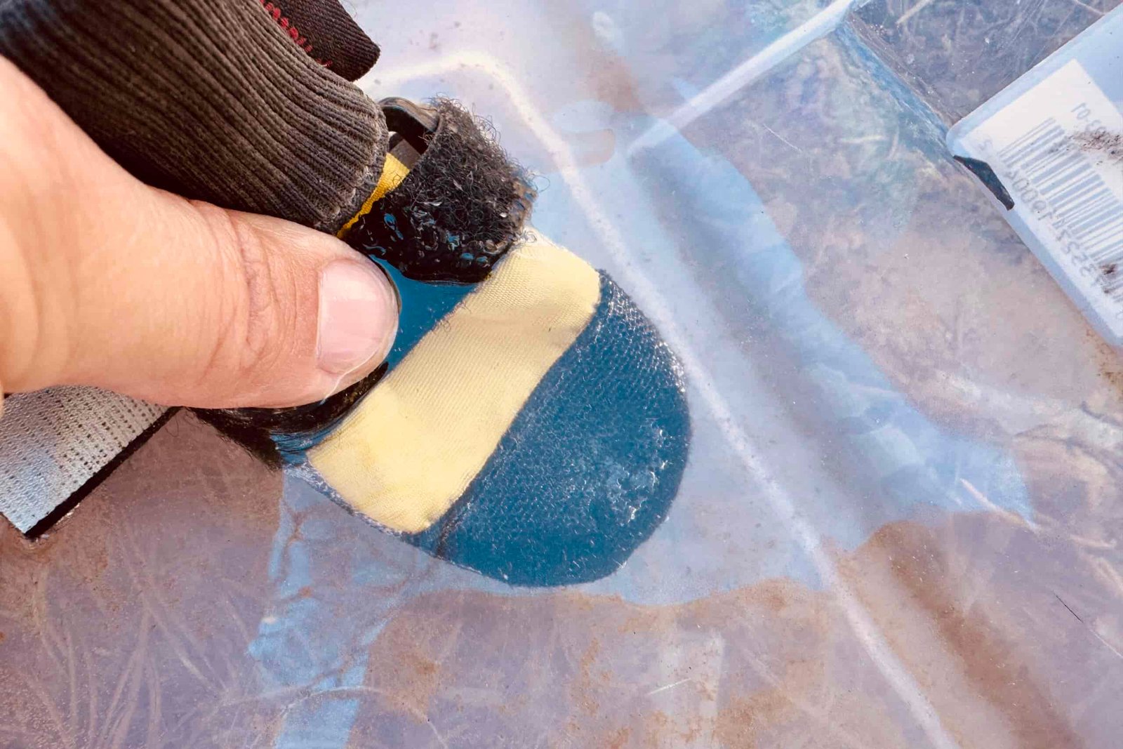 A close up of a person's hand dunking a Muttluks boot into a clear, plastic container of water.