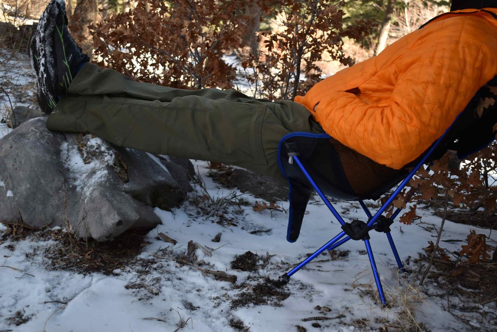 a hiker sits in a snowy campground on top of the Moon Lence Chair with his legs up on a rock