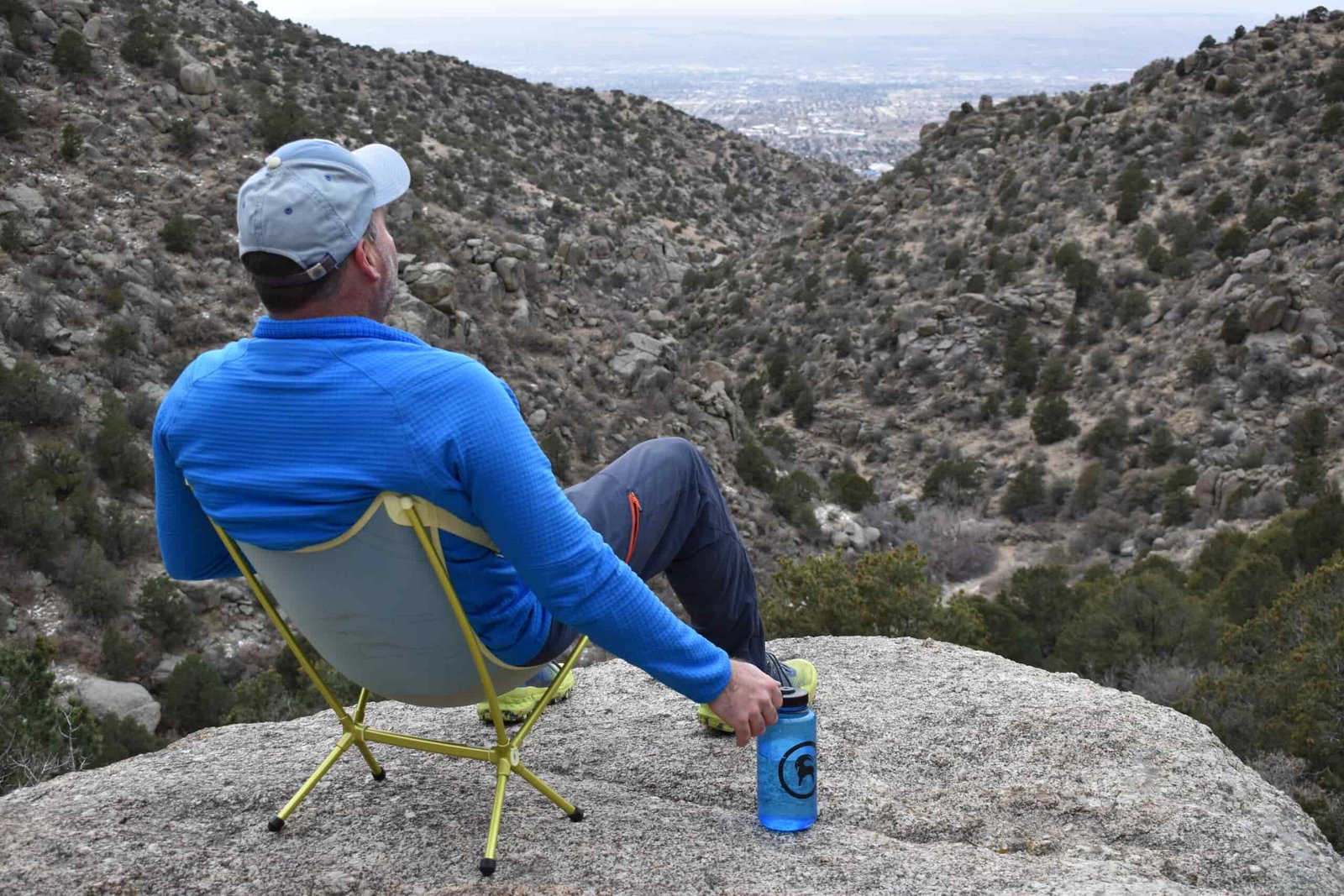 back view of a hiker sitting in a small backpacking chair at the edge of a scenic desert vista
