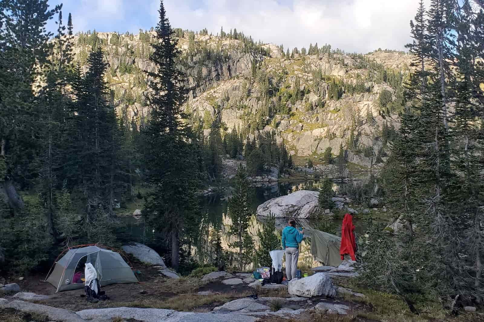 A woman stands in camp next to a lake.