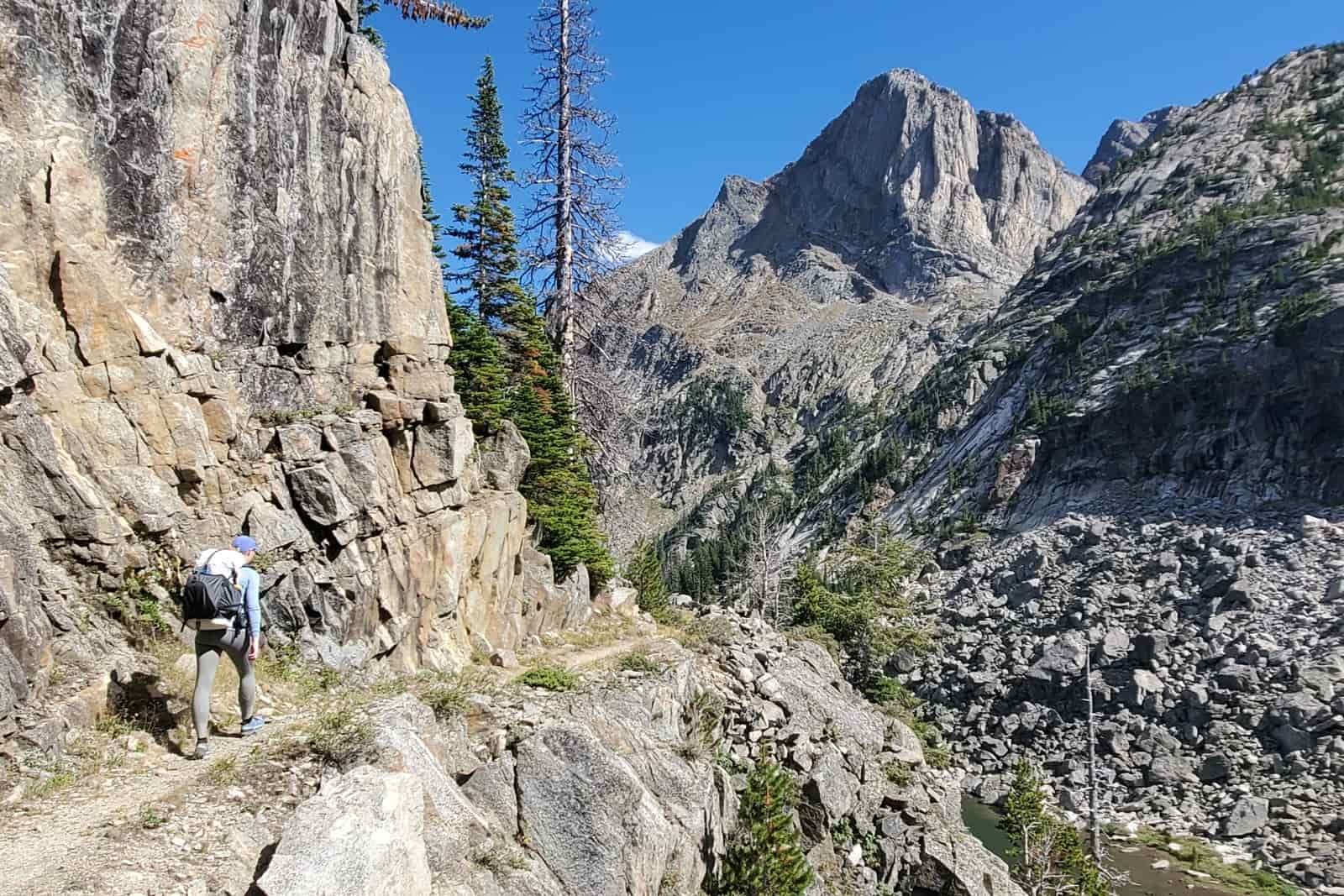 A woman hikes along a cliff edge with mountain views.