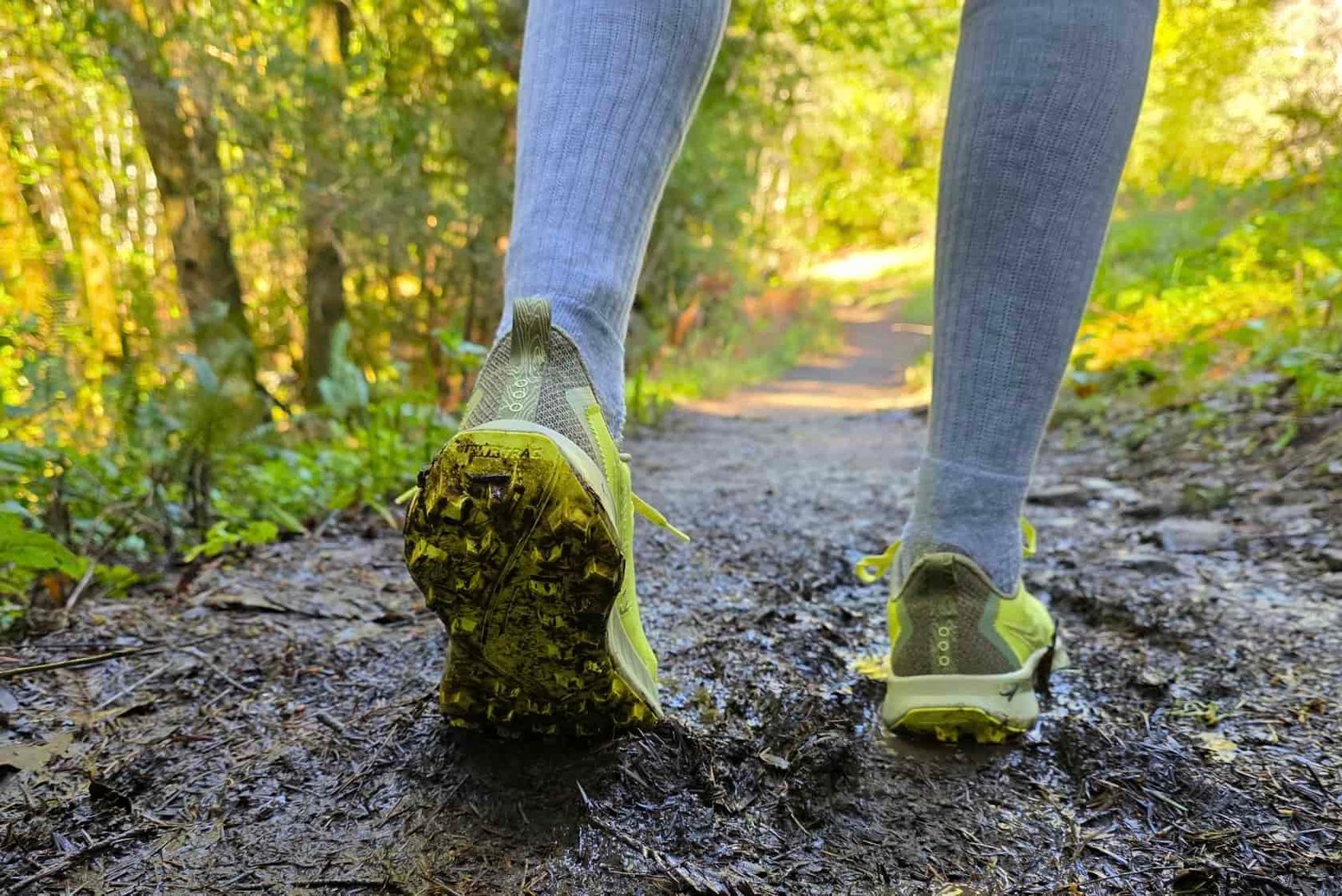 Close-up of the tread on the bottom of the Saucony shoes as a hiker hikes along a muddy trail.