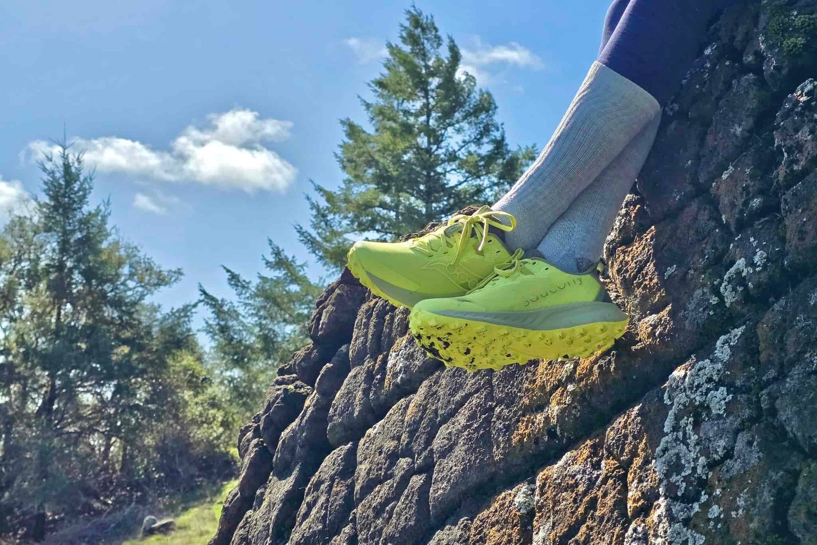 Hiker sitting on a large rock outcropping with a focus on the shoes that she is wearing.