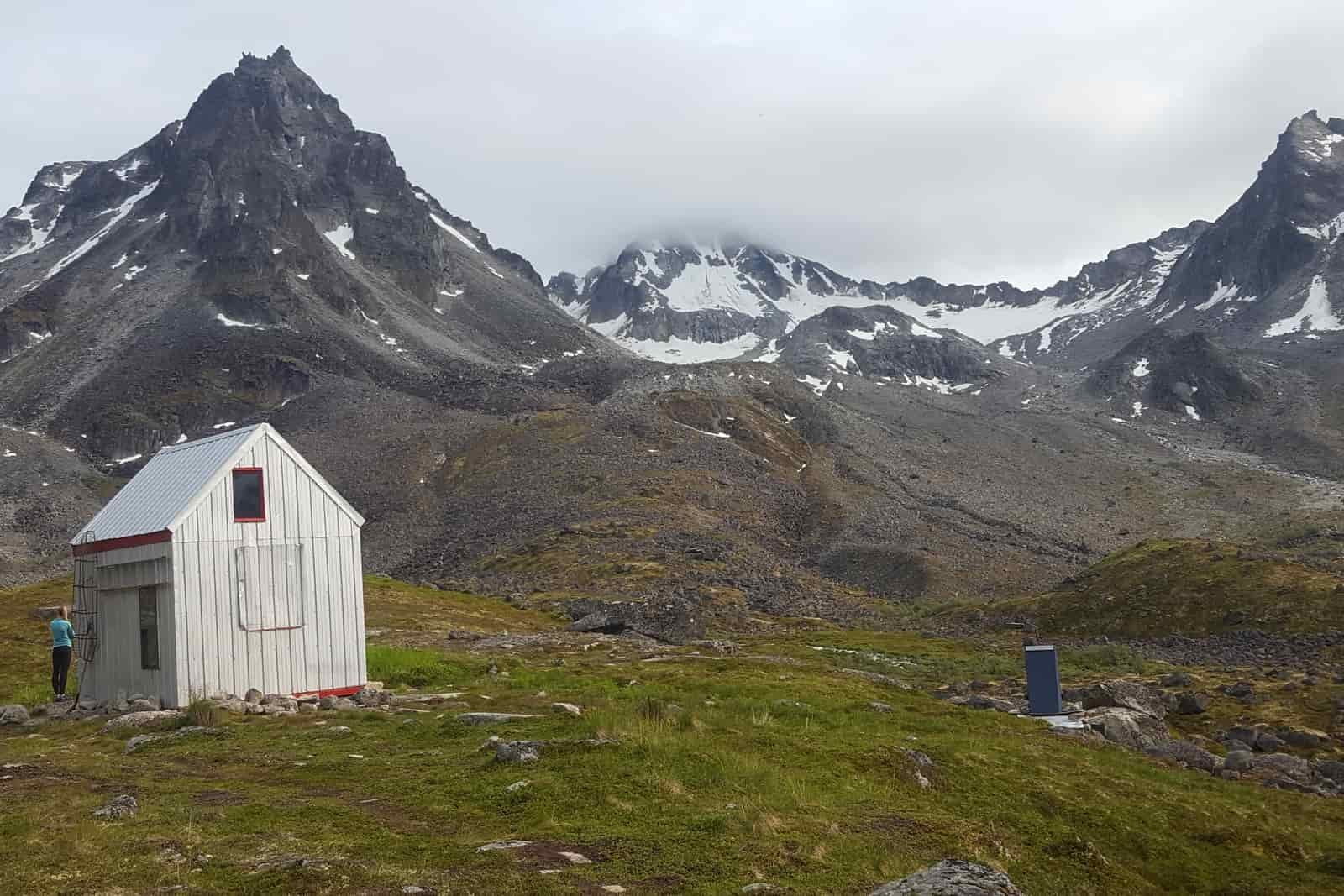 A mountain hut with soaring peaks in the background.