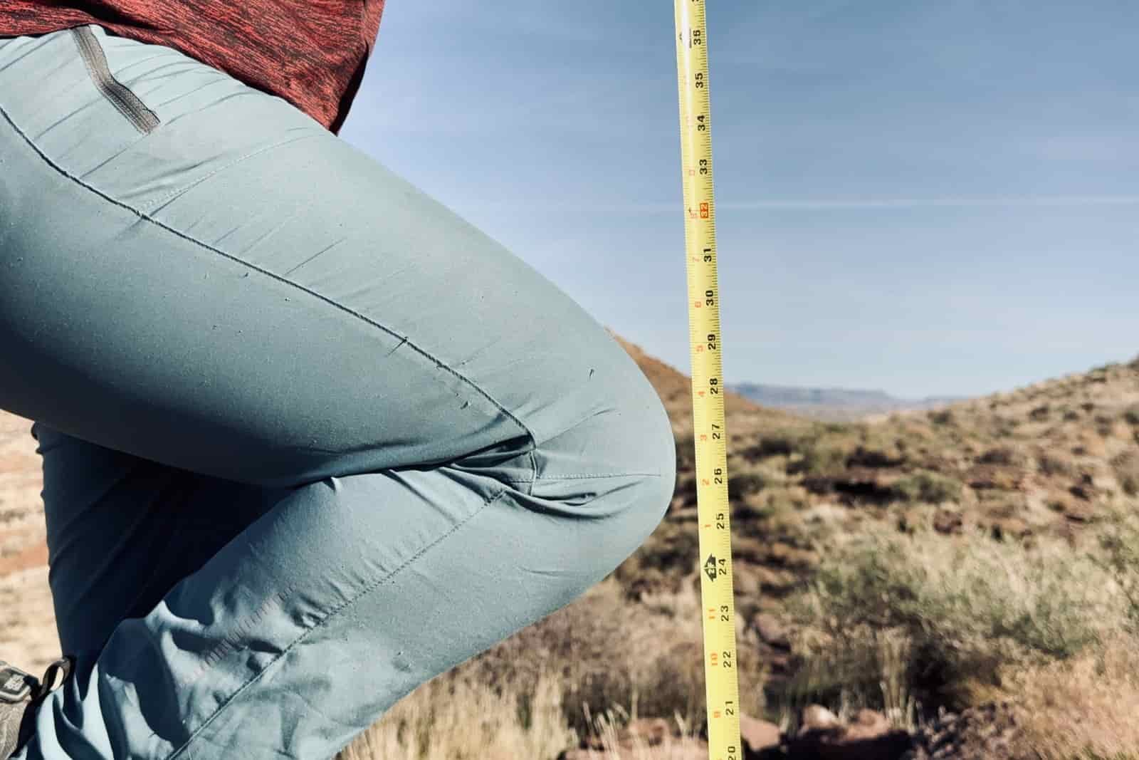 Close up of a measuring tape that is extended towards the ground next to a bent knee.