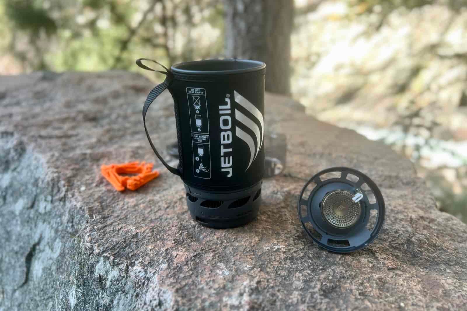 The jetboil flash and its components sit on a rock in a forest