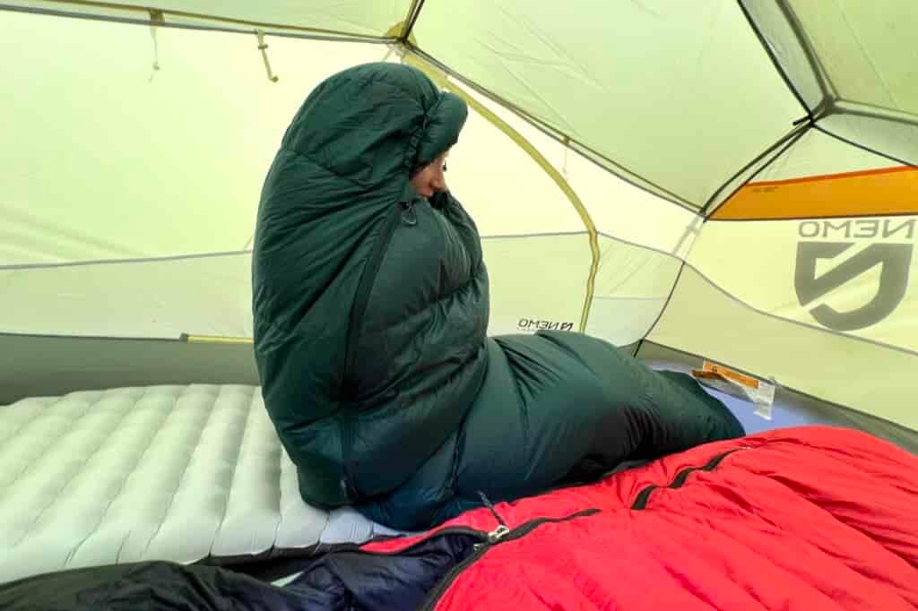 a hiker sits up in a tent, wrapped cozily in a sleeping bag