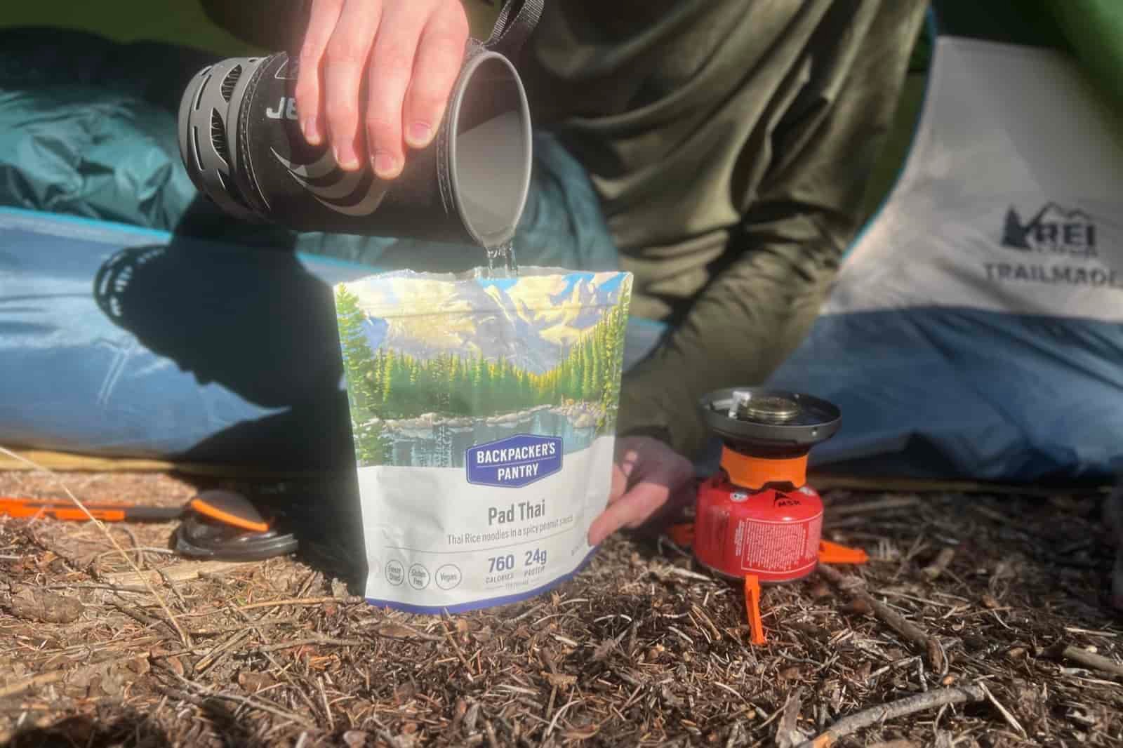 a closeup of a hiker's hand pouring water from the jetboil flash into a backpacker's pantry meal.