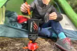 A closeup of a hiker sitting in a tent and stirring food in the jetboil flash.