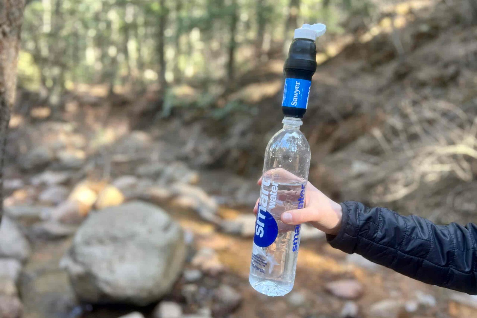 A hand holds a smartwater bottle with the sawyer squeeze attached