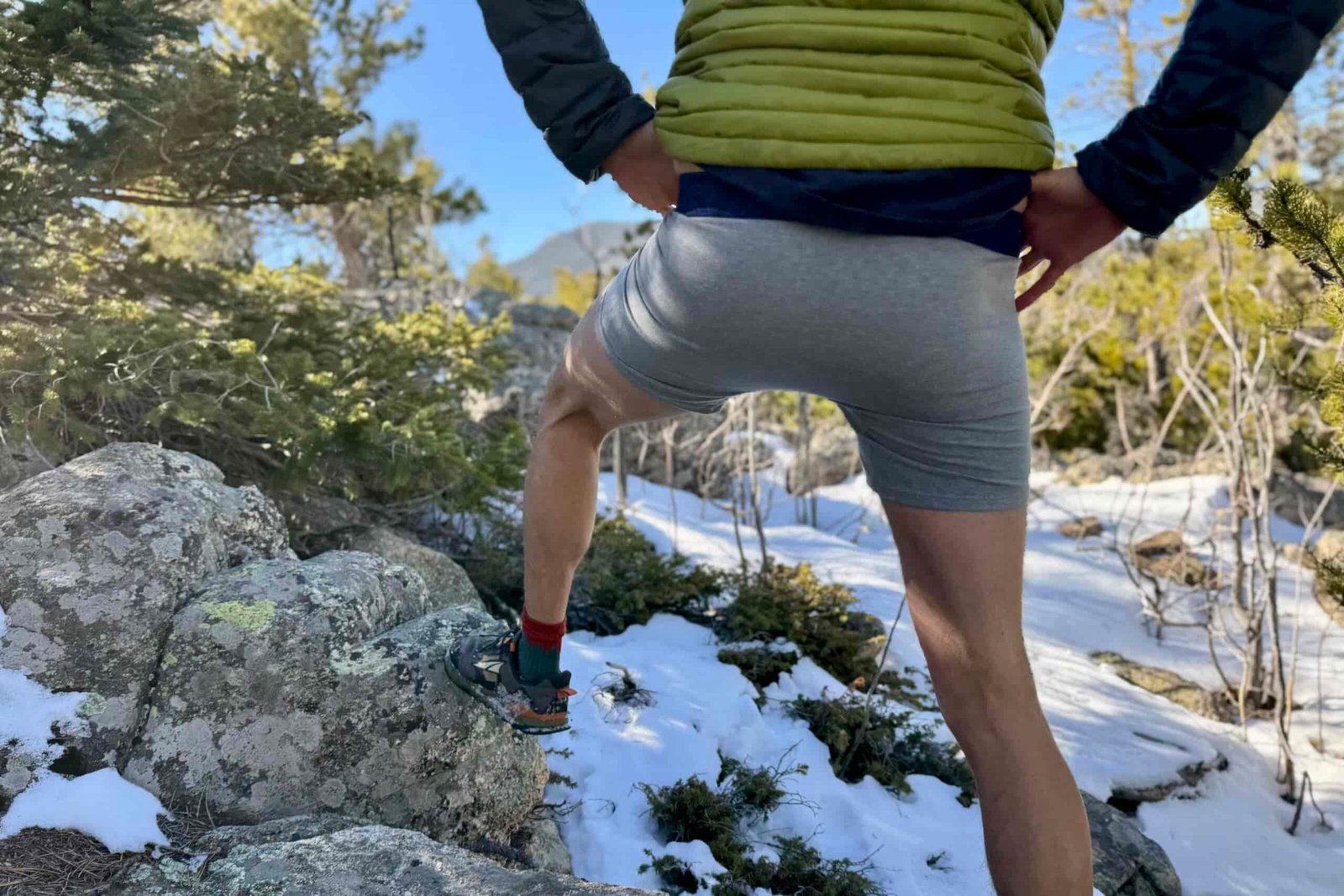 A hiker steps up on a rock with his pants off wearing a pair of under armour underwear.