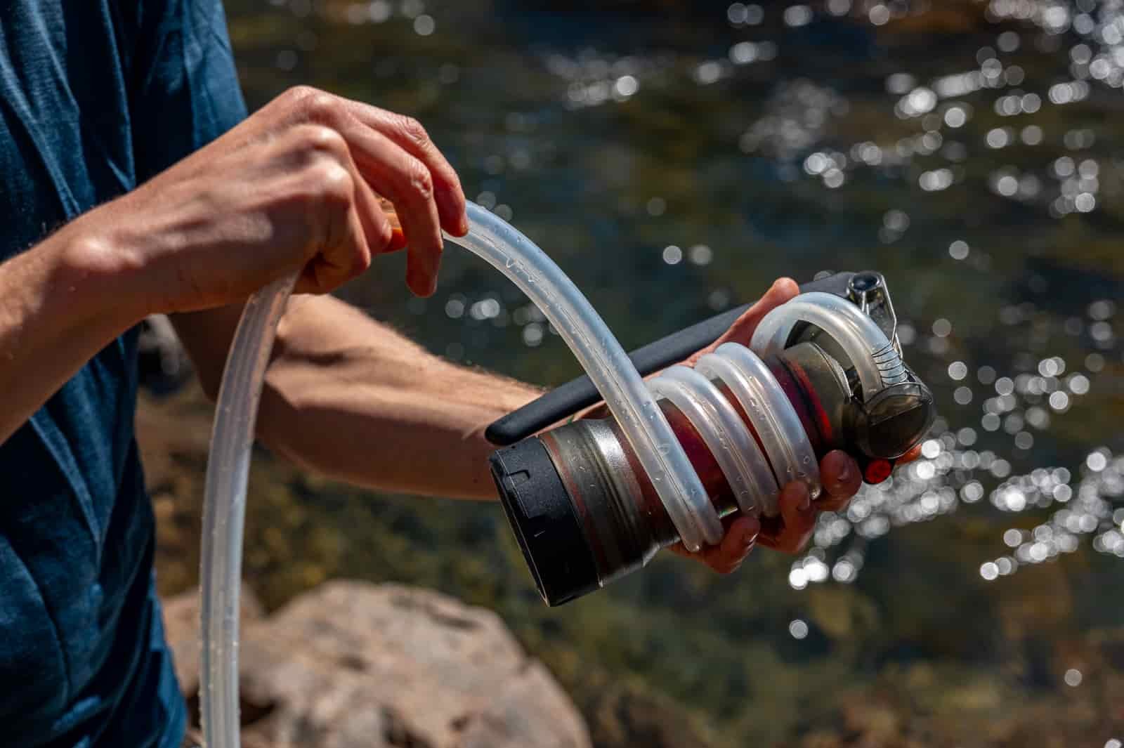 A close up of a hiker wrapping a water filter's hose around its housing.