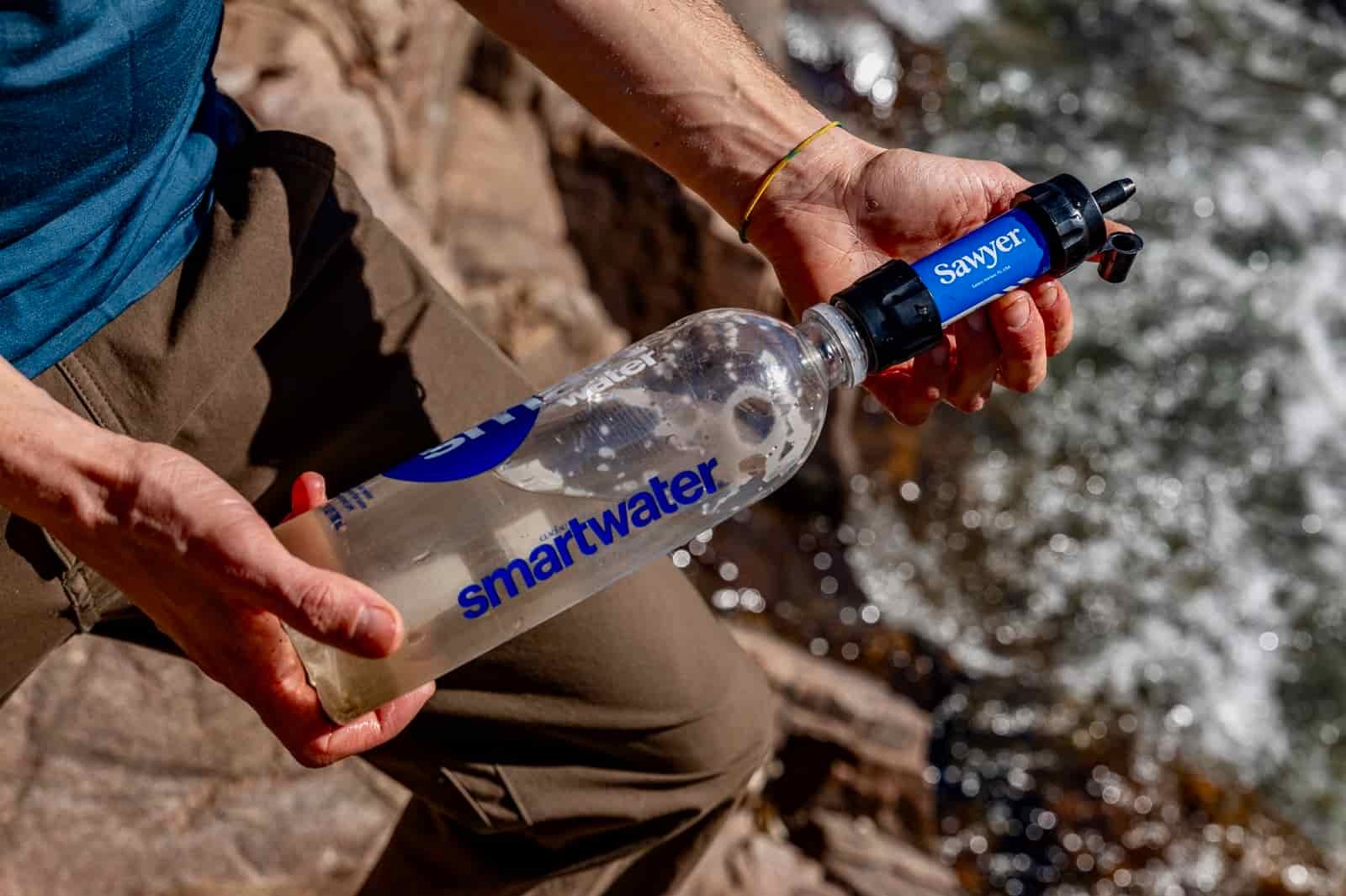 A hiker holds a smartwater bottle with the sawyer mini attached