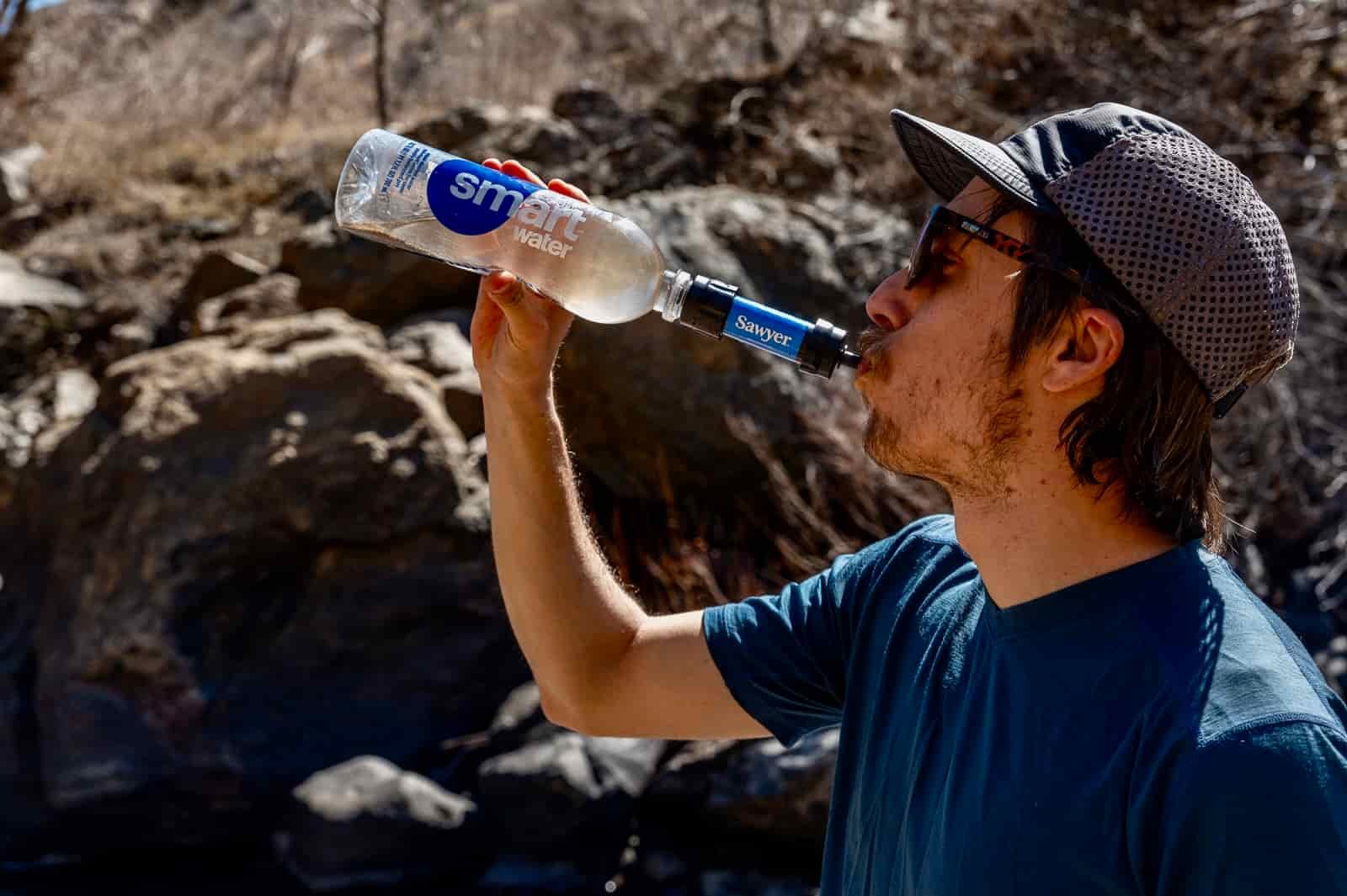 A hiker drinks from the sawyer squeeze attached to a plastic bottle.