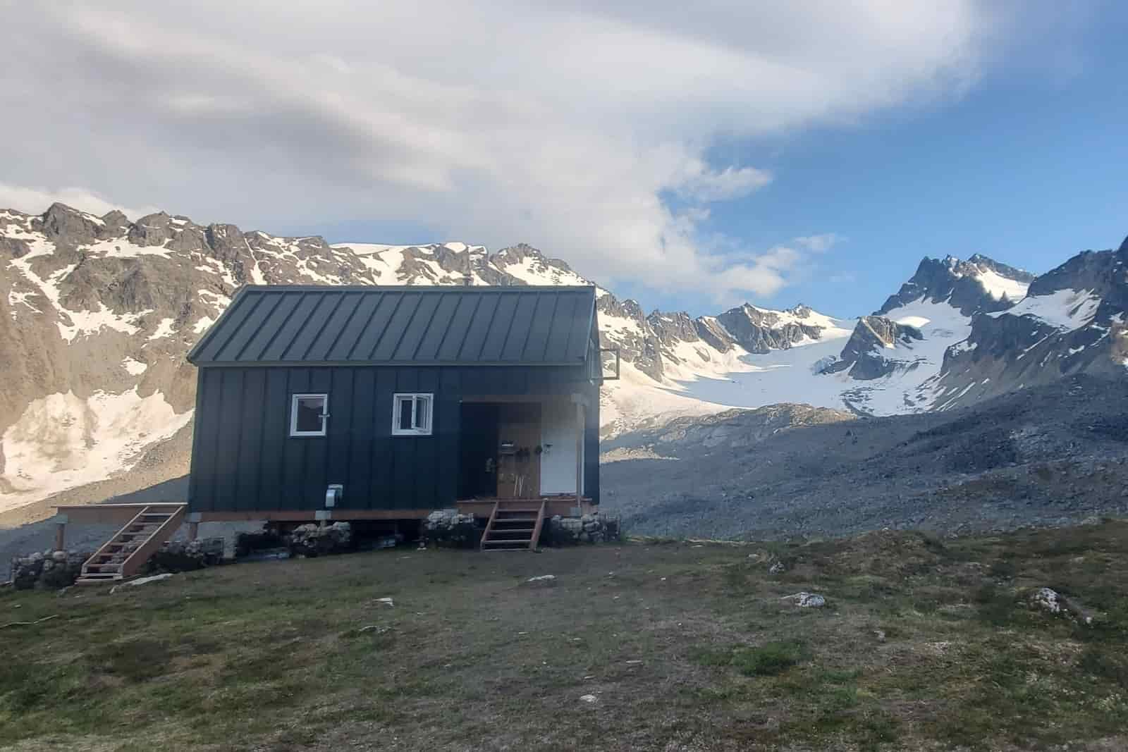 A green mountain hut with a glacial view.