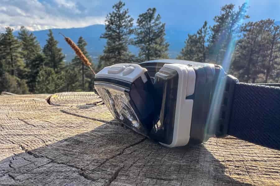 A side view of a headlamp sitting on a tree stump in a forest. There is a solar flair across the photo.