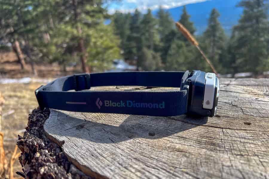 A headlamp sits on a tree stump in the forest. The Black Diamond name is showcased on the headlamp's strap.
