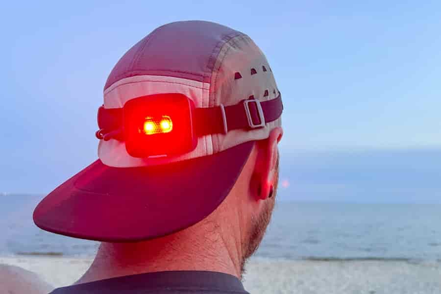 The back of a man's head showcasing the rear light of a headlamp. The light is illuminated red.
