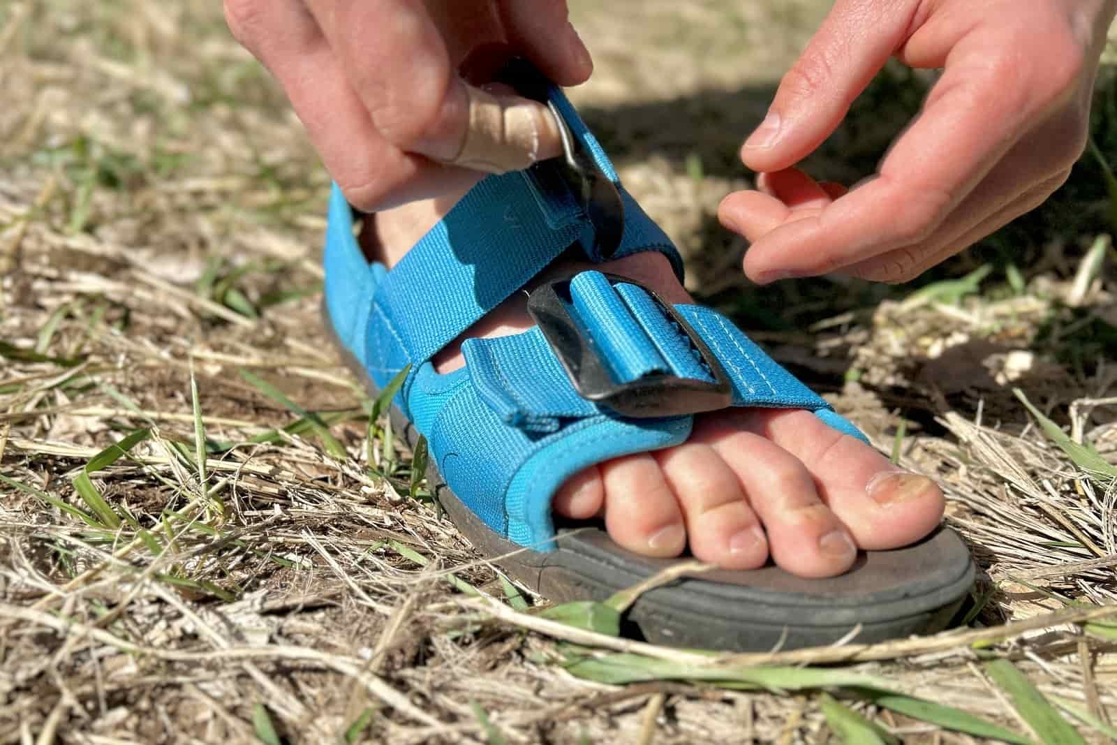 Close up image of a foot in a sandal with two hands adjusting the straps