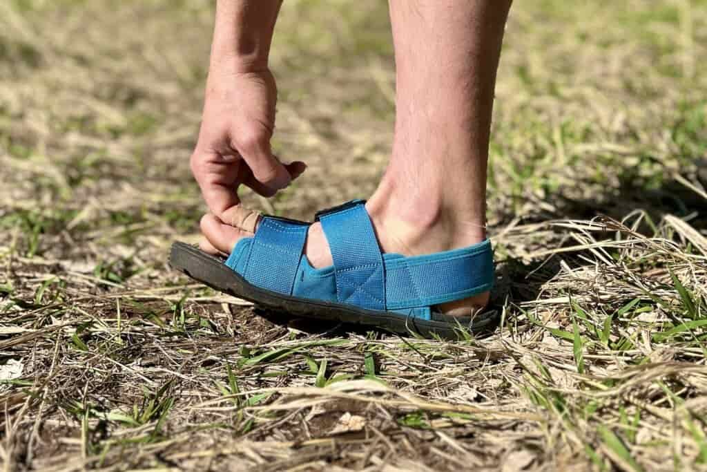 Close up image of a person's hand pulling on the front strap of a sandal.
