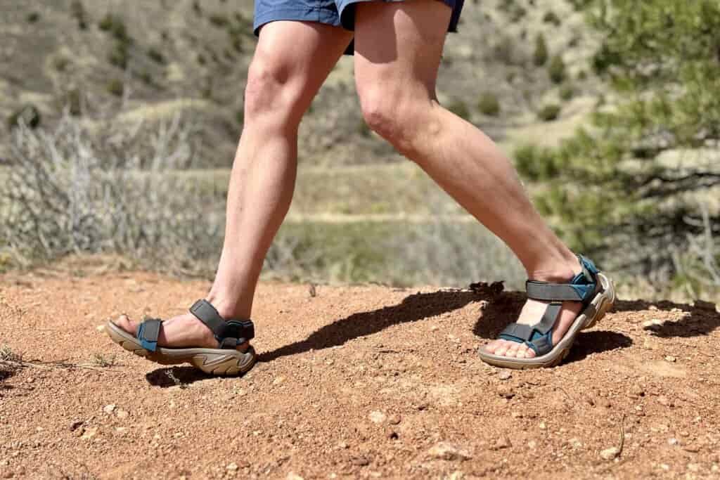 Close up image from the thigh down of a man walking in a pair of hiking sandals