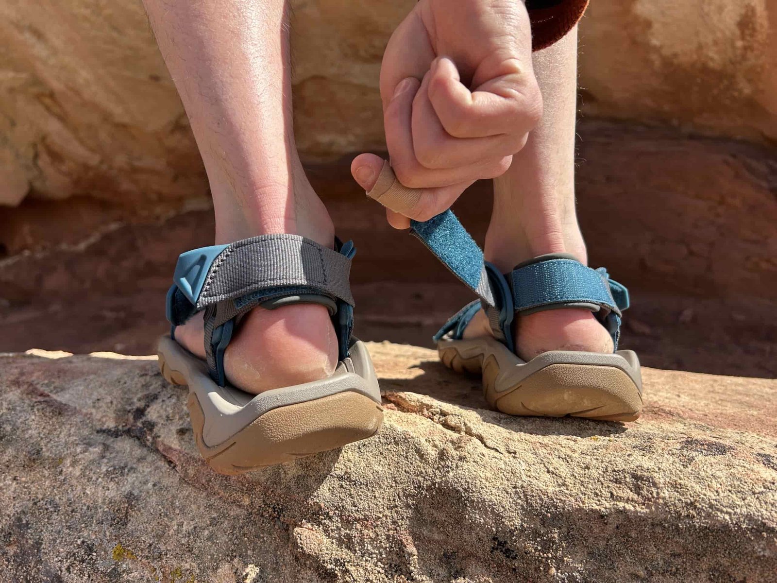 Close up image of two hands adjusting the heel tabs on a pair of hiking sandals