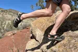 Close up image of a person wearing shorts and sandals stepping up on a steep rock.
