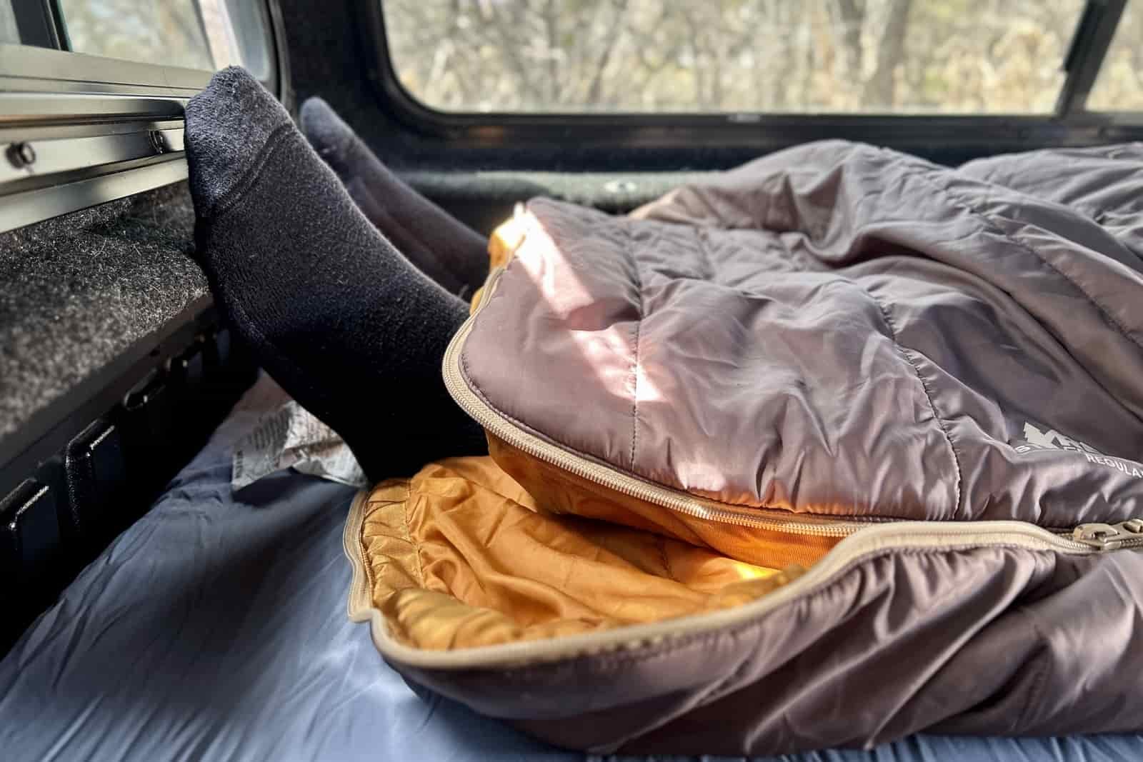 Two feet stick out of the bottom of a sleeping bag that's partially unzipped.