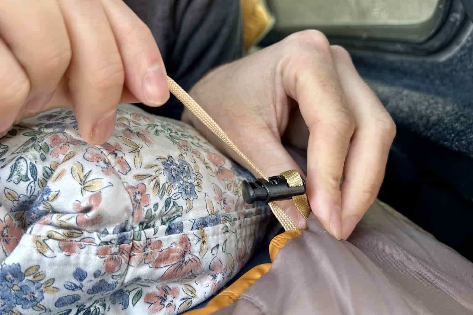 Close up image of a pair of hands adjusting the cord on a sleeping bag.